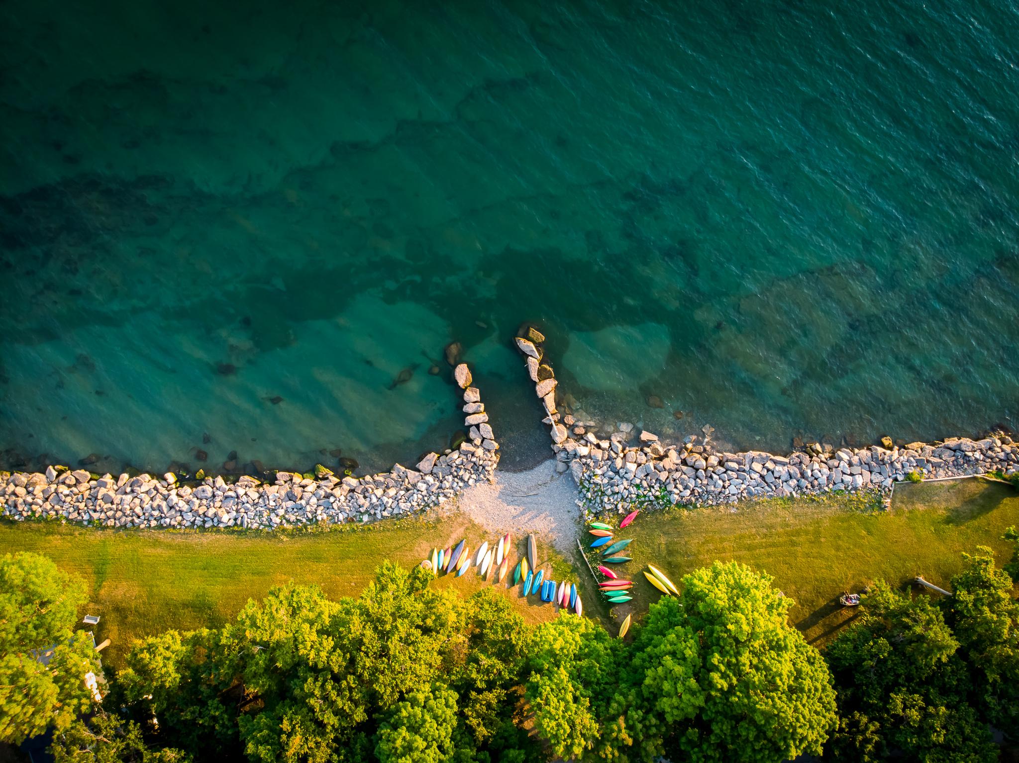 航拍的湖岸图像，海岸线上有岩石，彩色的独木舟和明亮的蓝绿色的水