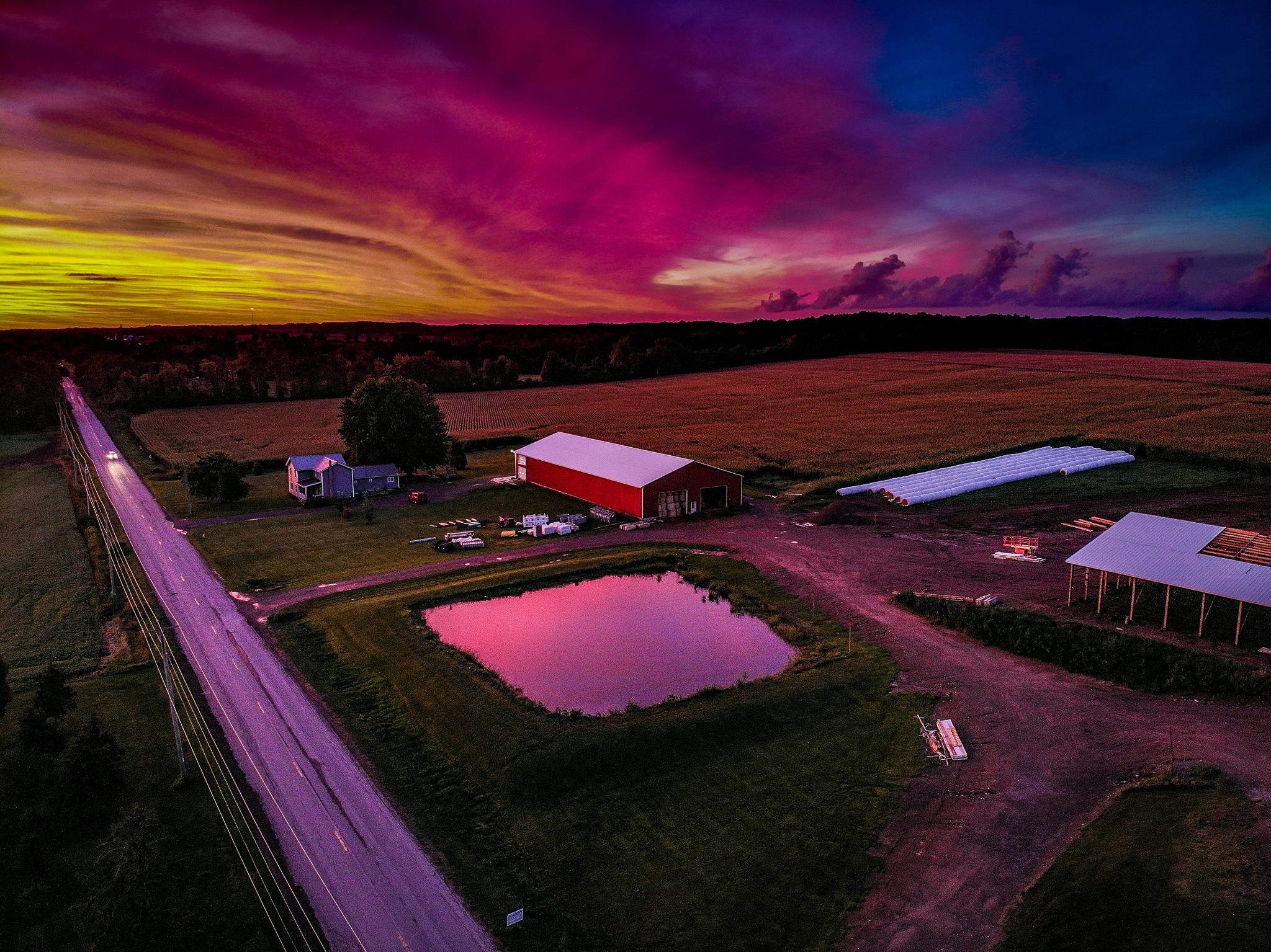 农场的航拍照片，中心是池塘和五颜六色的日落